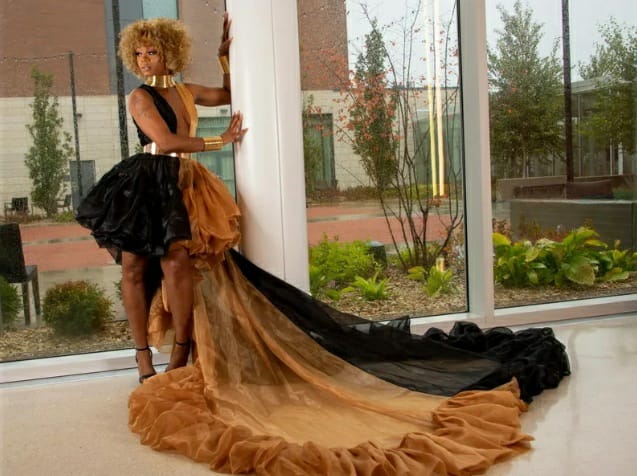 Black and bronze gown with a structured bodice, gold choker and cuffs, a bubble hem and an expansive layered tulle train spread across the floor