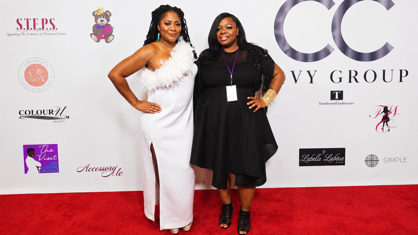 Therese Marie in a black dress with a beaded shawl and a VIP pass, posing with a guest in a white feather-trimmed gown on the S.T.E.P.S. red carpet