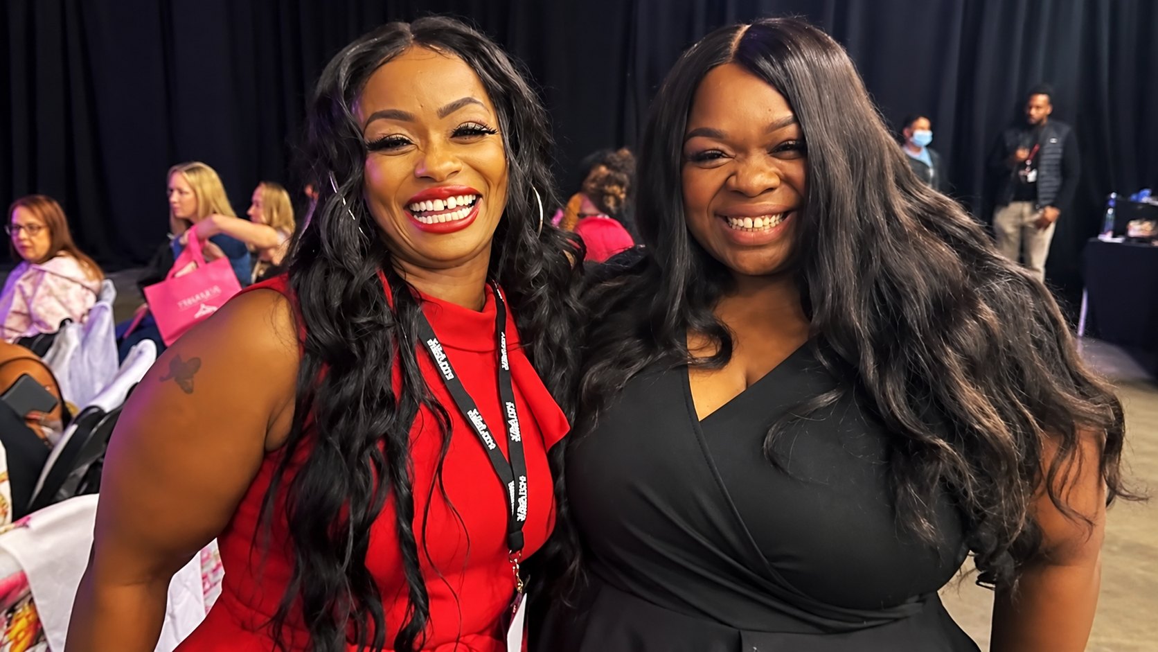 Therese Marie in a black wrap dress smiling beside a guest in a red dress at a fashion event