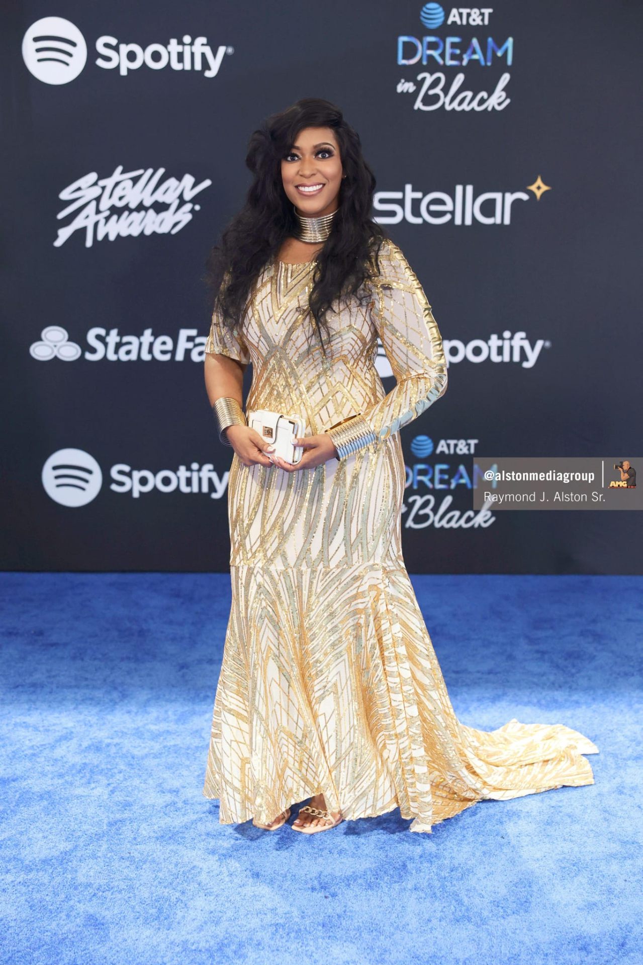 Cream champagne floor-length gown with gold sequin geometric patterning and a slight mermaid flare, on a blue event carpet