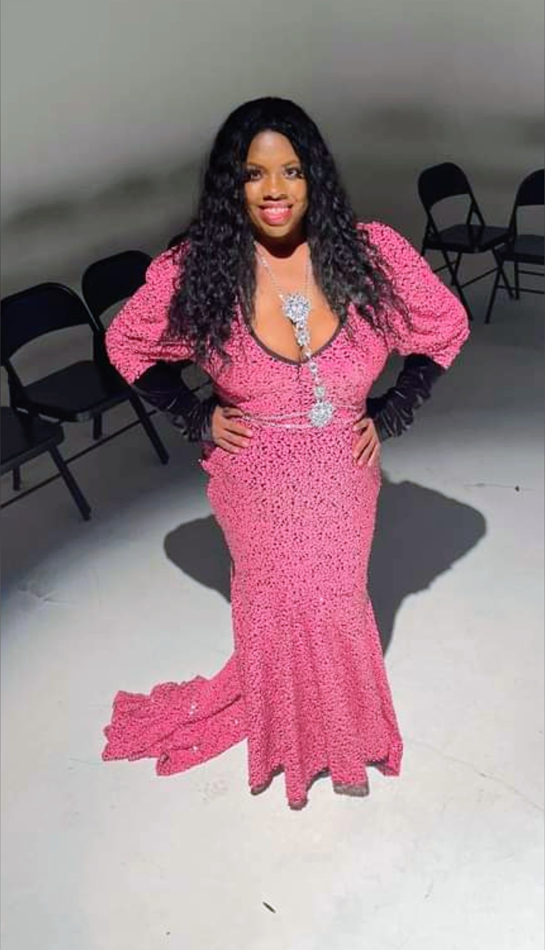 Pink sequin mermaid gown with puff sleeves, black velvet gloves and a crystal drop necklace, in a spotlit studio