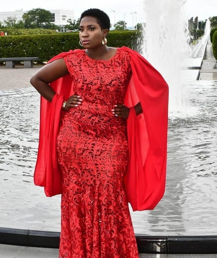 Red lace gown with flowing cape sleeves beside a fountain